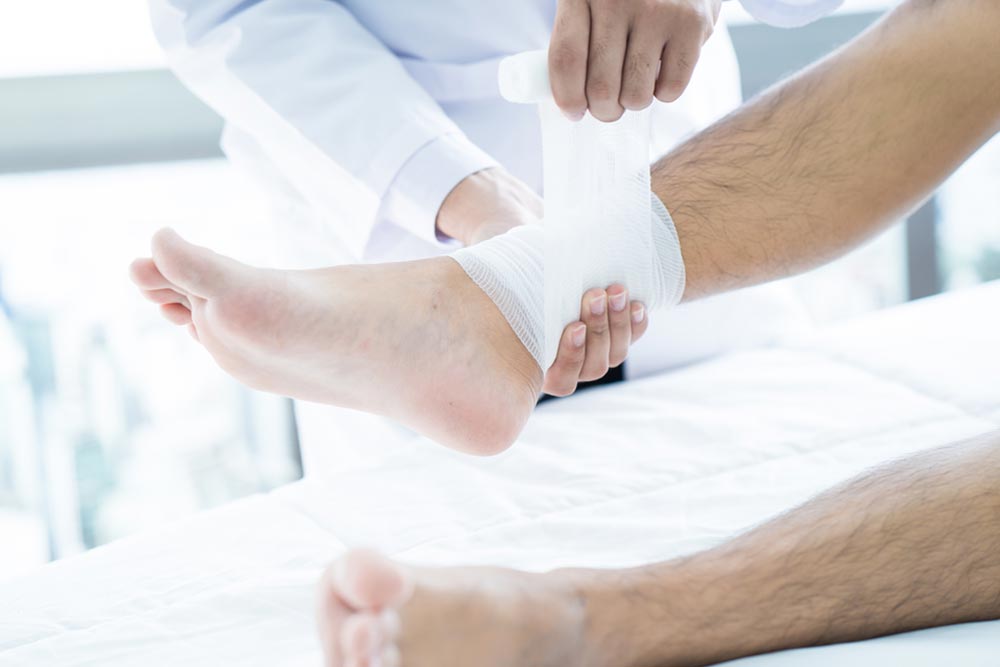 Close-up of male doctor bandaging foot of patient at doctor's office.