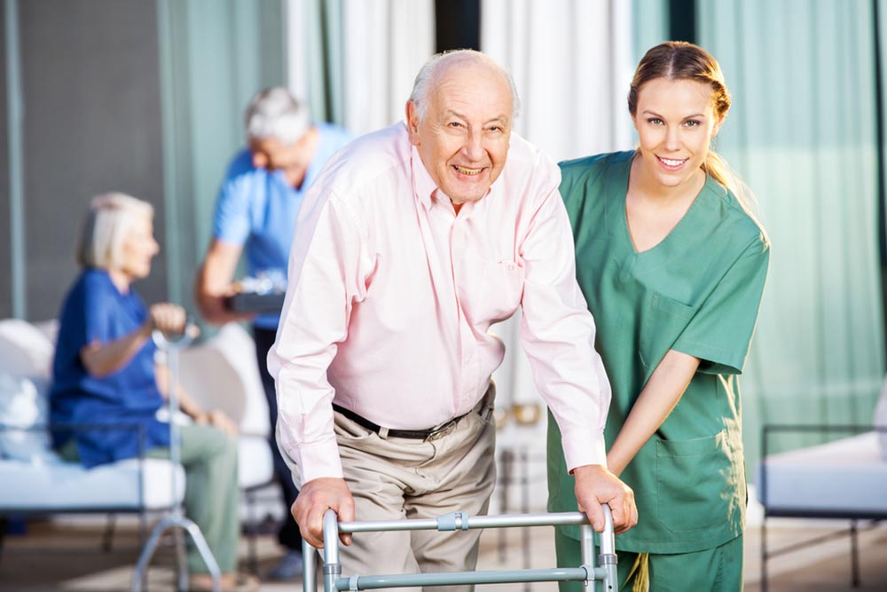 Portrait of happy female caretaker helping senior man in using Zimmer frame at nursing home yard